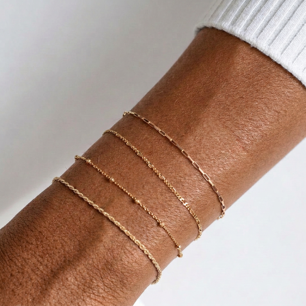 Four delicate gold chain bracelets layered on a wrist